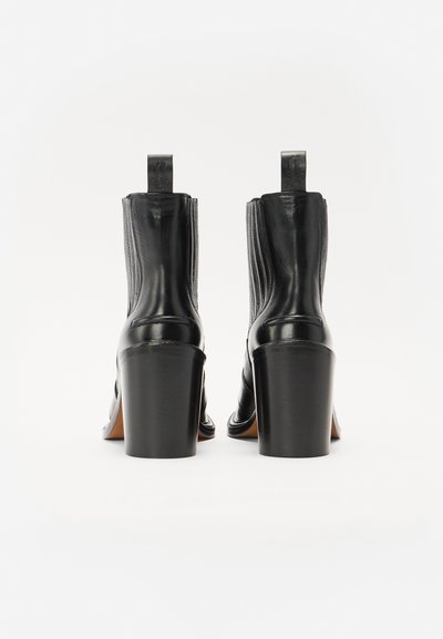 Botas de tobillo de cuero negras con un acabado texturizado, tacones de bloque altos y lengüetas traseras, que presentan costuras verticales a lo largo de los lados.