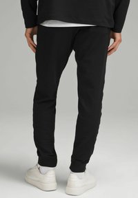 Zwarte joggingsbroek van zacht materiaal met elastische boorden. Gemaakt met witte sneakers met een getextureerd ontwerp en zichtbare veters.