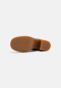 Suela de zapato negra con una parte inferior de goma marrón claro, que presenta un diseño plano y una textura sutil; sin logotipos ni patrones visibles.