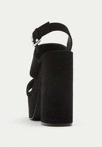 Black suede heeled sandals with a thick platform, open back, and adjustable ankle strap. Smooth texture with a matte finish.