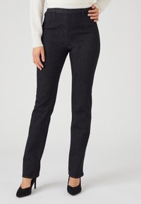 Pantalones de mezclilla de lavado oscuro con una silueta ajustada, cintura alta y detalles de costura mínimos, combinados con zapatos de tacón negro.