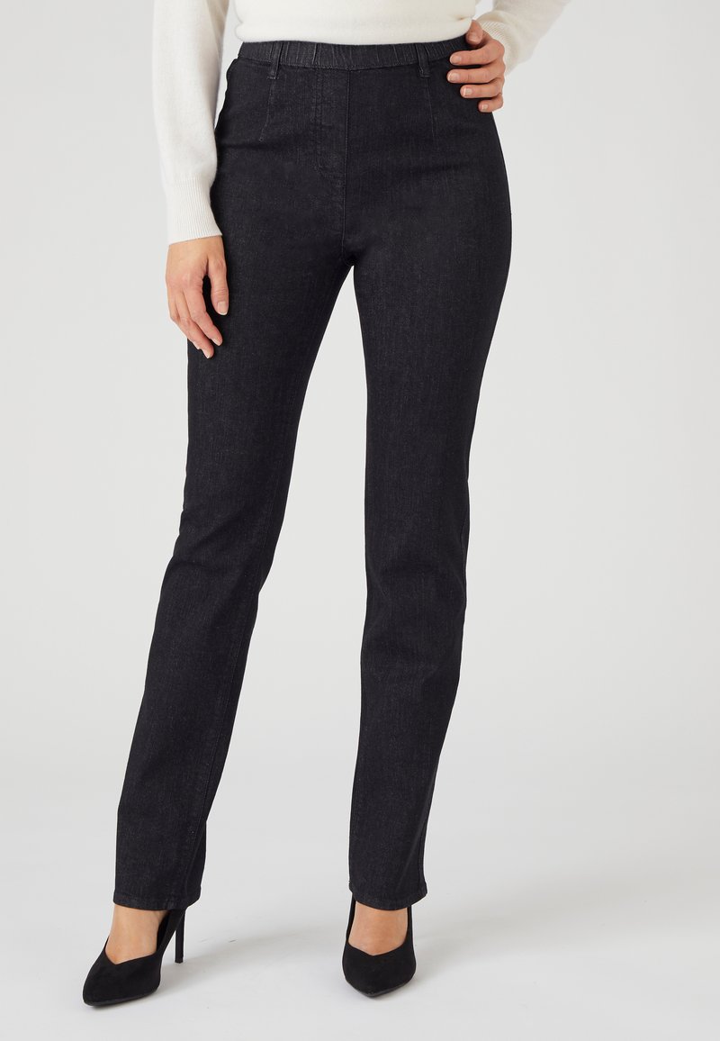 Pantalones de mezclilla de lavado oscuro con una silueta ajustada, cintura alta y detalles de costura mínimos, combinados con zapatos de tacón negro.