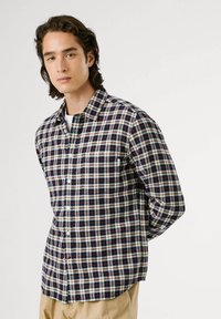 Camicia con bottoni in un motivo a quadri blu navy, rosso e crema; maniche lunghe; taschino frontale; il tessuto ha un aspetto morbido e strutturato.