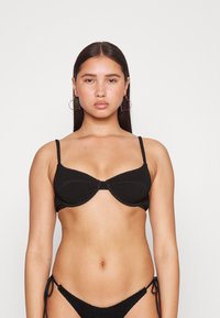 Top de bikini preto com tecido texturizado, suporte com arame, alças finas e ajustáveis, e um fundo de bikini preto correspondente com laterais amarráveis.