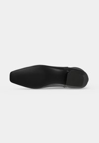 Semelle d'une chaussure habillée noire avec un bout pointu et des zones texturées au talon et à l'avant-pied pour l'adhérence, présentée sur un fond clair uni.