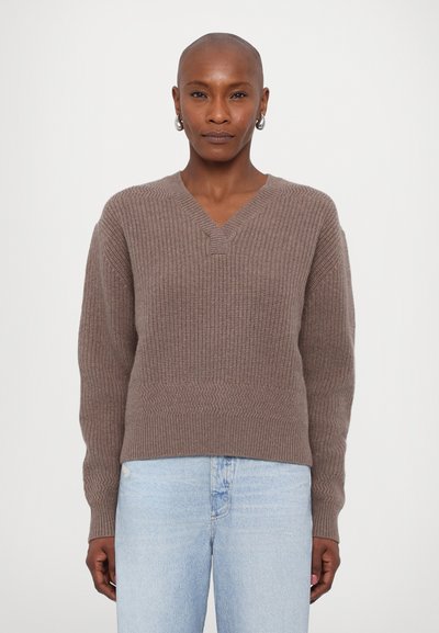 Brown knitted sweater with a V-neck, ribbed texture, and long sleeves. Worn with light blue jeans, showing a relaxed fit.
