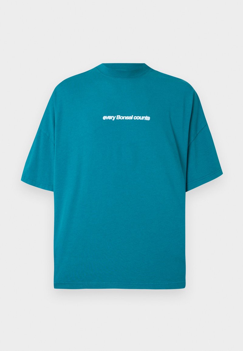 T-shirt en coton bleu-vert avec une coupe décontractée, un col rond et des manches courtes. Présente un texte blanc "chaque Bonsal compte" sur le devant.