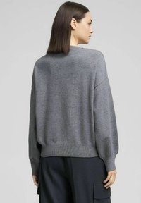 Maglione grigio in maglia con vestibilità ampia, spalle scese e orlo a coste. La texture è liscia, con un design semplice e minimalista.