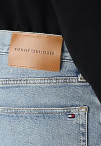 Világoskék farmernadrág bőr címkével, amelyen a "TOMMY HILFIGER" felirat látható, valamint egy kis piros, fehér és kék logó a hátsó zseben.