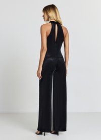 Combinaison noire sans manches avec un corsage ajusté, un pantalon à jambes larges et un détail dos en forme d'œillet, fabriquée dans un matériau doux et velouté.