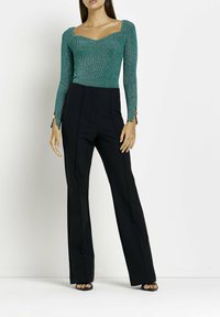 Tållblå, långärmad, figurnära tröja med fyrkantig halsringning och texturerad tyg; tillsammans med högmidjade, svarta, vida byxor.