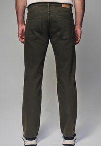 Donkergroene broek van stevige stof, met een recht model, twee achterzakken en een tan leren label op de tailleband.
