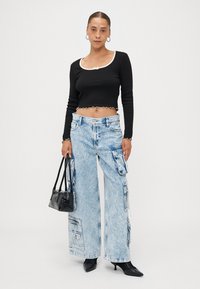 Black cropped top with a cream trim, paired with light blue wide-leg cargo jeans featuring multiple pockets and zippers. Black handbag, pointed heels.