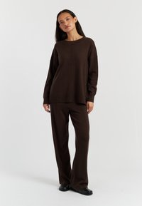 Bruine gebreide trui met een relaxte pasvorm en lange mouwen, gecombineerd met bijpassende bruine wijde broek. Soepele textuur, minimale details.