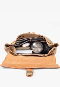 Canvas and leather bag open showing notebooks, white wireless earbuds case, stainless steel water bottle, and black wallet inside.