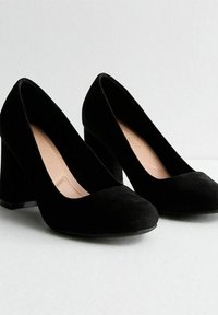 Scarpe con tacco alto in camoscio nero, con punta arrotondata e tacco spesso, caratterizzate da una texture liscia e un design semplice.