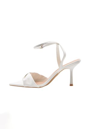 Sandalo bianco con tacco alto, punta appuntita, cinturino frontale arricciato, sottile cinturino alla caviglia con fibbia e tacco a spillo su sfondo bianco.