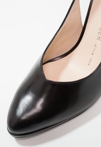 Escarpin en cuir noir avec un bout pointu et un design découpé. Texture lisse, couture minimale et doublure intérieure beige.