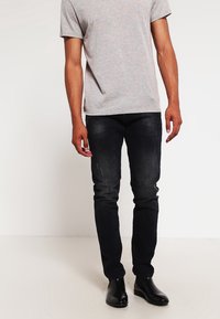 Mörkblå jeans med slim fit, med blekta områden och subtila veck, i kombination med en ljusgrå t-shirt med kort ärm.