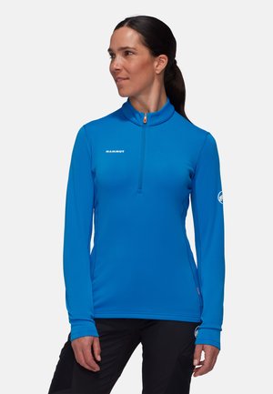 Blauwe sportieve top met lange mouwen en een halve ritssluiting, gemaakt van soepel stof, met logo van het merk op de borst en mouw, en een oranje ritsaccent.