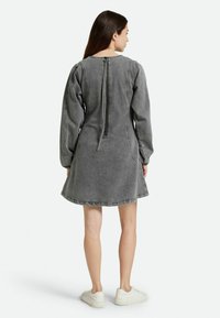Vestido de mezclilla gris con forma acampanada, mangas largas y cremallera en la parte trasera. Presenta costuras sutiles y un escote redondeado.