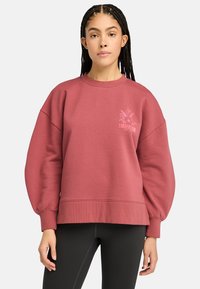 Maroon huppari, jossa on löysä malli, ribatut hihansuut ja helma. Vasemmassa rinnassa on kukkakuviollinen Timberland-logo. Pehmeä kangastuntuma.