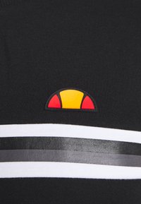 Chemise en coton noire avec un logo caoutchouté aux accents rouges, jaunes et noirs. Trois bandes horizontales en blanc, gris et noir.