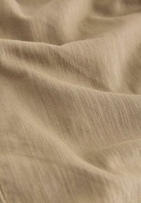 Tissu beige avec une texture fine de tissage diagonal et des plis doux et fluides créant des ombres douces.