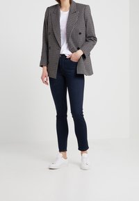 Svart och vit houndstooth dubbelknäppt blazer, vit t-shirt, mörka slim-fit jeans och vita sneakers. Rena linjer och strukturerad passform.