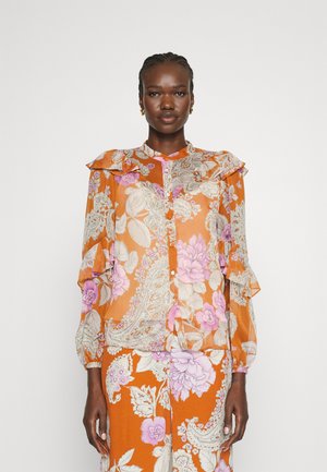 Blusa arancione traslucida con motivi floreali paisley in rosa e bianco, presenta spalline arruffate e chiusura a bottoni sul davanti.