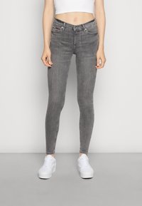 Jeans skinny de denim gris con cintura alta, que cuentan con bolsillos delanteros y un discreto detalle de logo. Combinados con zapatillas blancas.