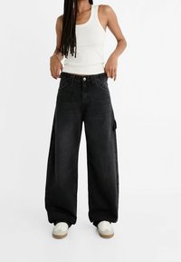 Loszittende zwarte denim jeans met een hoge taille, knoopsluiting, voorzakken en zijzakken met klep. Gecombineerd met witte sneakers.