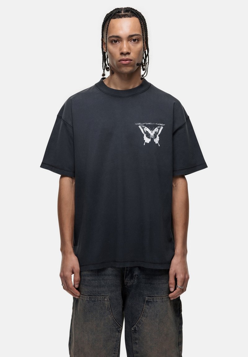 Zwarte oversized katoenen t-shirt met een witte vlinderafbeelding op de linkerborst. De stof heeft een zachte, gladde textuur.