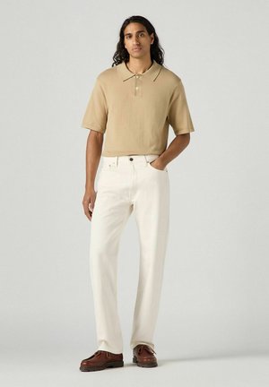 Tan short-sleeve polo shirt with a collar, paired with loose-fitting white jeans and brown lace-up shoes. Smooth texture and casual design.