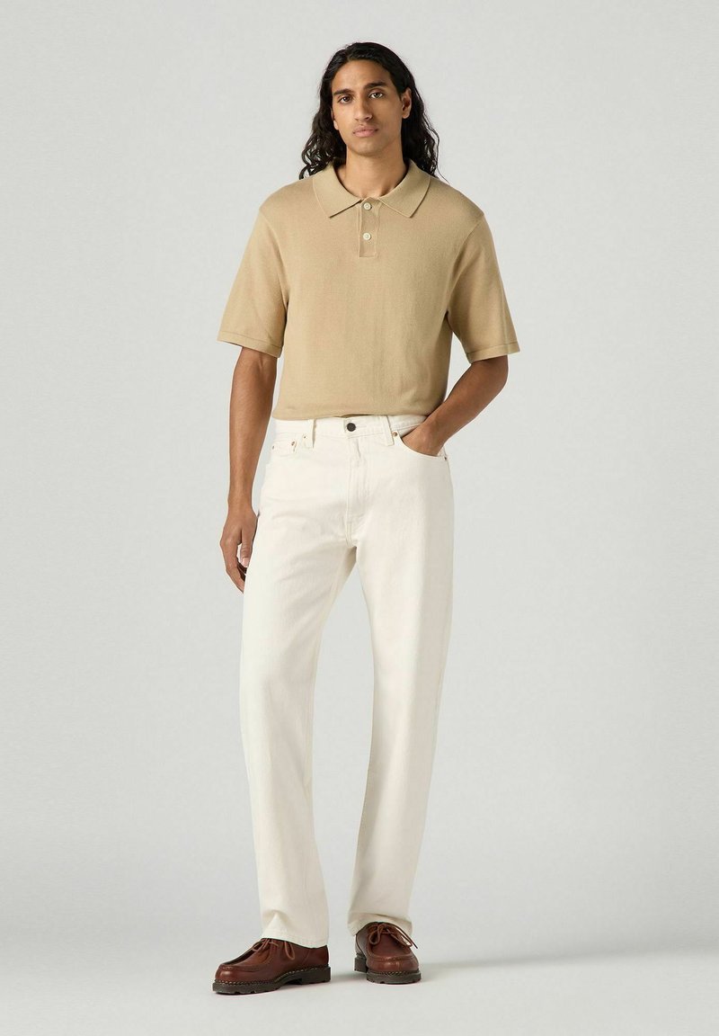 Tan short-sleeve polo shirt with a collar, paired with loose-fitting white jeans and brown lace-up shoes. Smooth texture and casual design.