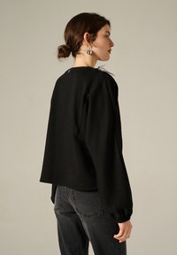 Felpa nera con vestibilità rilassata, caratterizzata da maniche lunghe a palloncino e scollatura tonda. Il materiale ha una texture morbida.