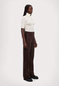 Hvit ribbet kortermet turtleneck, kombinert med brune vide bukser med sideakenter, båret med svarte platåsko.