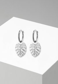 Orecchini a cerchio in argento con un pendente a forma di foglia dettagliato e con motivi intagliati. Il design testurizzato enfatizza la forma della foglia e le sue linee naturali.