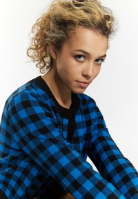 Cardigan a scacchi blu e neri con bottoni neri rotondi, tessuto testurizzato e colletto e polsini neri a costine, progettato per un look aderente.