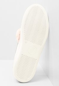 Biały sneaker z teksturowaną gumową podeszwą, z wzorem zygzaka i różowym futrzanym akcentem po boku, w pobliżu tylnej części.