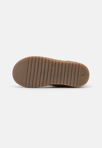 Suola di scarpa in gomma marrone con un motivo di presa testurizzato e scanalature orizzontali. Dettaglio del logo circolare vicino al tallone. Design piatto e materiale durevole.