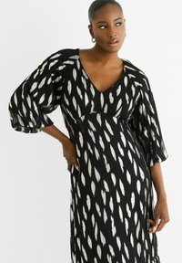 Black dress featuring a V-neck, puff sleeves, and a silver abstract pattern. The fabric has a lightweight, textured appearance.