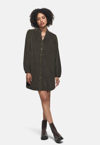 Vestito button-up in corda di colore verde oliva con colletto arricciato, maniche lunghe e vestibilità comoda, abbinato a stivali neri alla caviglia.