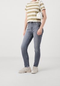 Camiseta corta a rayas verdes y blancas, jeans ajustados grises y zapatillas beige. Incluye un pequeño bolso blanco con textura suave y diseño curvado.