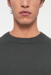 Szary sweter z dzianiny o ryflowanej fakturze, z okrągłym dekoltem i dopasowanym kształtem. Minimalistyczny design bez ozdób.