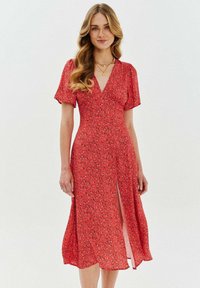 Červené květinové šaty s krátkými rukávy, výstřihem do V a předním rozparkem. Lehká tkanina s splývavým designem a rozptýlenými malými květy.