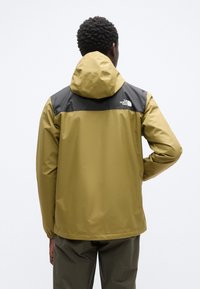 Αδιάβροχο μπουφάν σε ελιά πράσινο με μαύρο άνω τμήμα, με κουκούλα και ελαστικά μανίκια. Λογότυπο εμφανίζεται στην πλάτη.