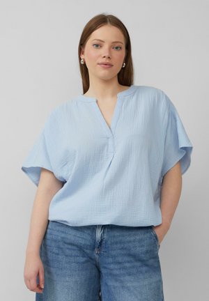 Blouse bleu clair à manches courtes en tissu texturé avec un col en V et une coupe décontractée, associé à un short en denim taille haute.