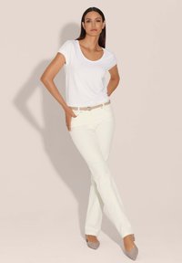 Witte t-shirt met ronde hals gecombineerd met lichte crèmekleurige flared jeans, geaccentueerd met een beige riem. Het model draagt lichtgrijze puntige ballerina's.