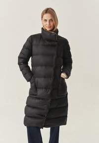 Giacca piumino nera con colletto alto, design a cuciture verticali, tasche laterali e accenti arancioni a contrasto lungo le cuciture.